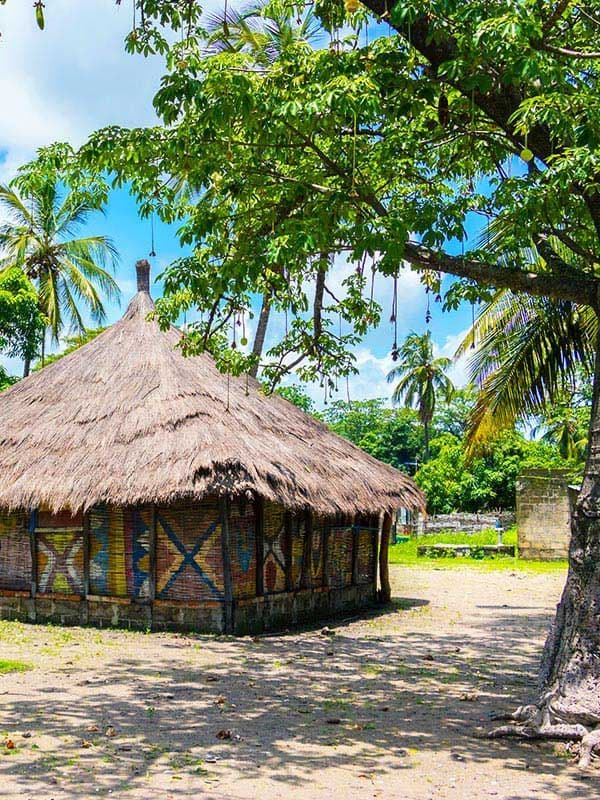 Case ronde aux murs peints et au toit de chaume entourée de palmiers en Casamance